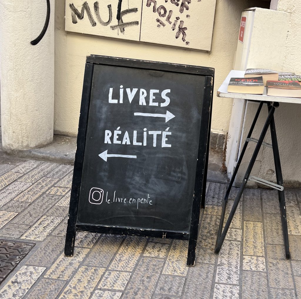 Bild einer Tafel vor einem Straßencafé : rechts geht's zu Livres und links geht's zur Réalité