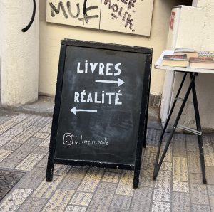 Bild einer Tafel vor einem Straßencafé : rechts geht's zu Livres und links geht's zur Réalité