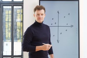 Ein Berater steht am Flipchart und schaut selbstbewusst in die Kamera